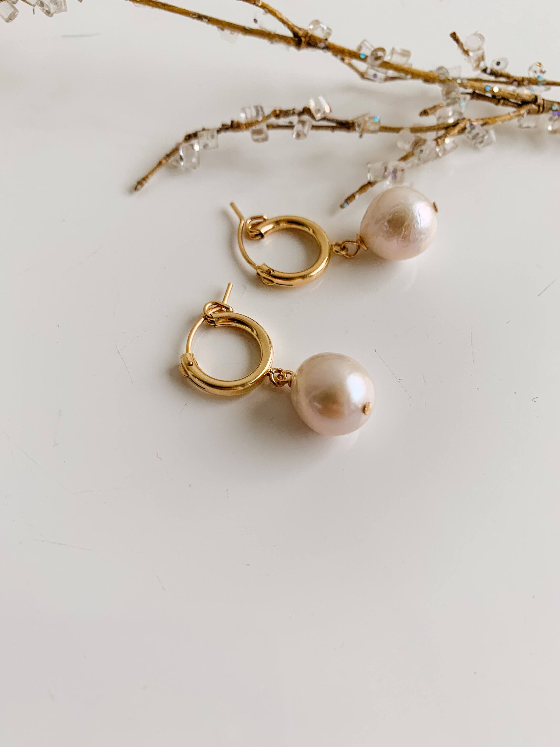 A pair of gold huggie hoop earrings with pearl drop
